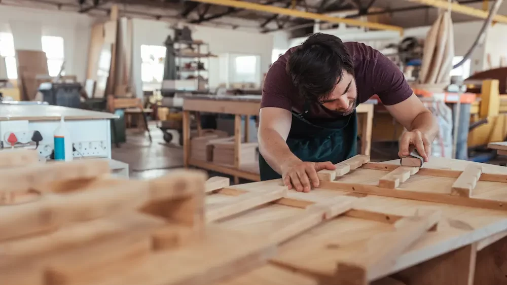 Skilled young carpenter with beard hand sanding