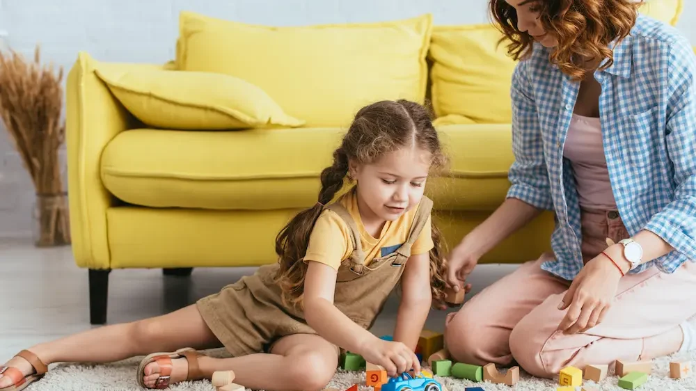 Young nanny sitting near adorable kid playing with toy car