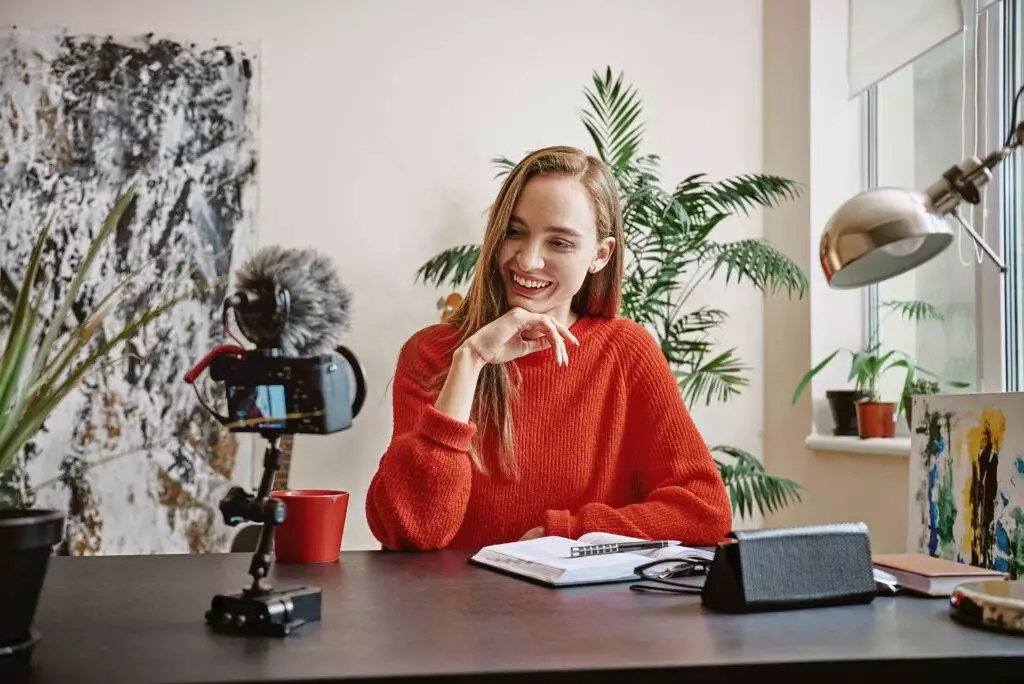 Female young vlogger recording social media video and smiling while looking at camera