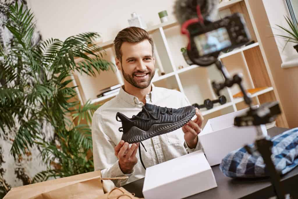 Cheerful male blogger holding black sneakers while recording new video for his blog.
