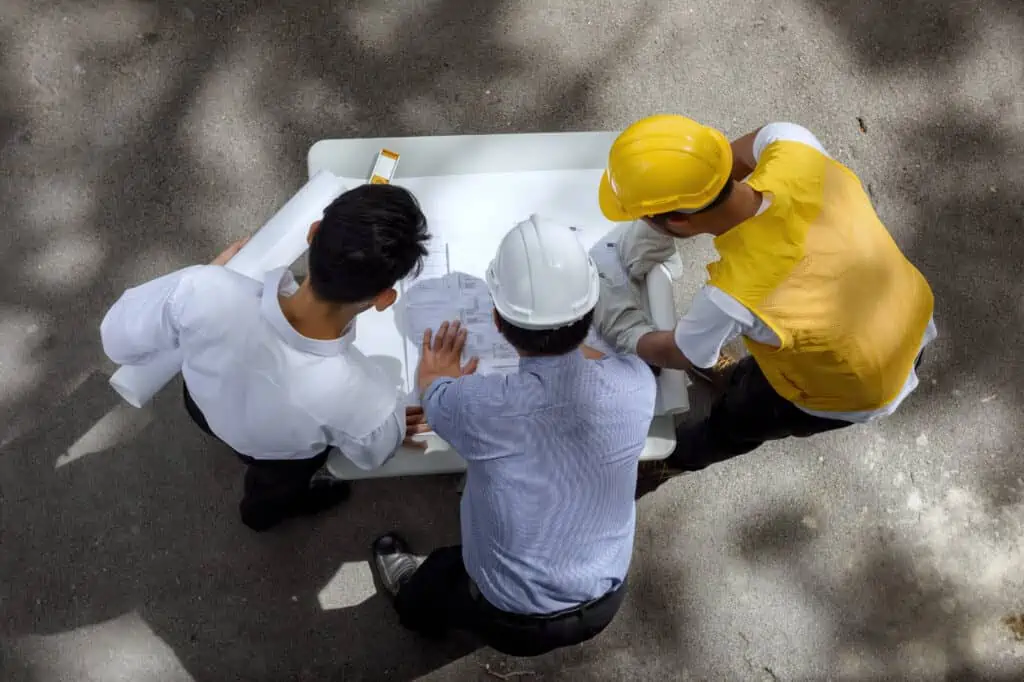 Top view of Engineering team of site manager, young field engineer, and foreman look paper blueprint to discuss projet at construction site, Concept for team work of heavy industry.