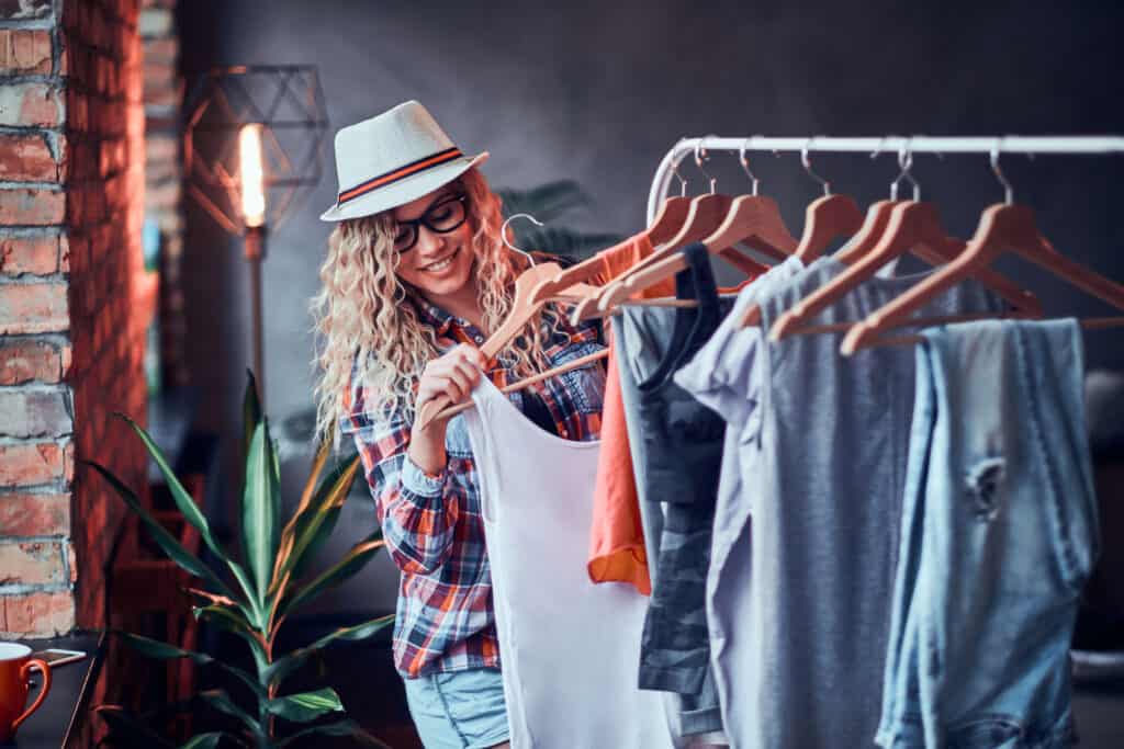 Pretty young woman in hat and glasses is choosing new outfit for summer