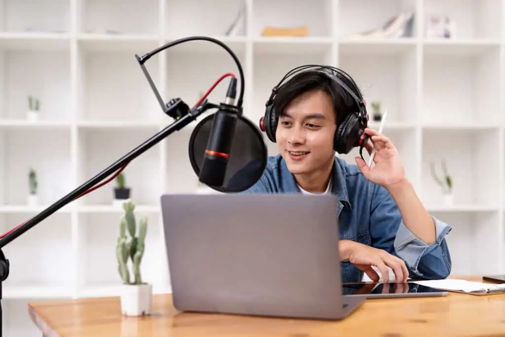 A man with headphones and a microphone in front of a laptop.