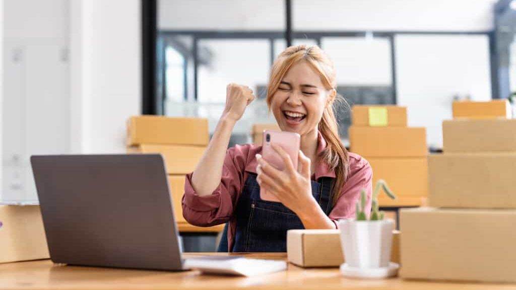 Happy young asian woman entrepreneur, Smile for sales success after checking order from online shopping store in a smartphone at home office, Concept of merchant business online and e-commerce.