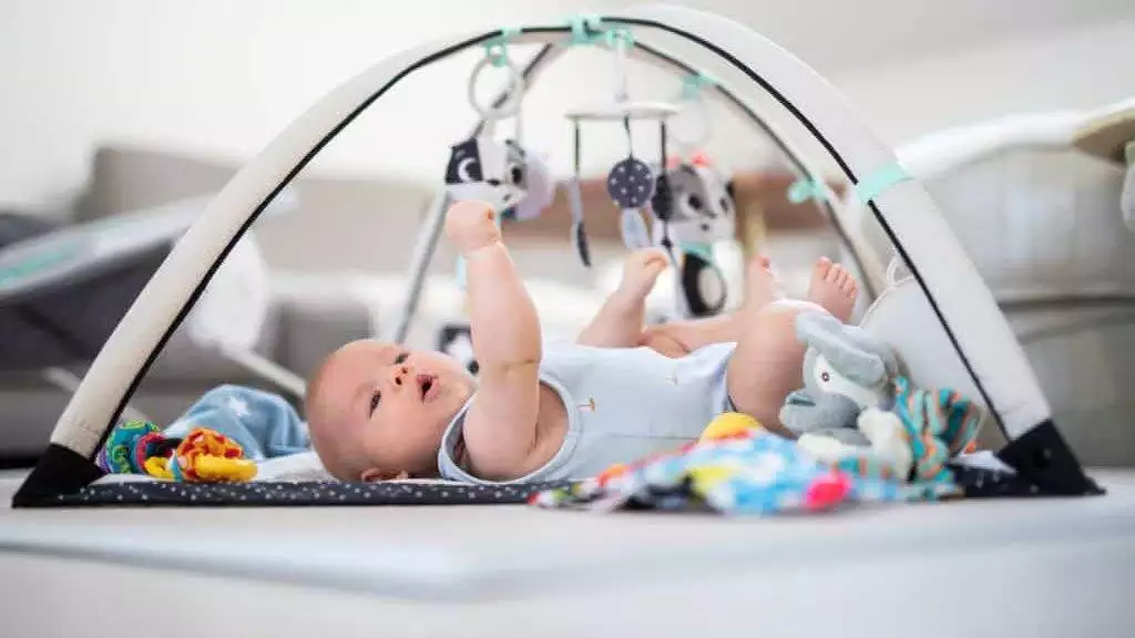 Cute baby boy playing with hanging toys arch on mat at home Baby activity and play center for early infant development. Baby playing at home.