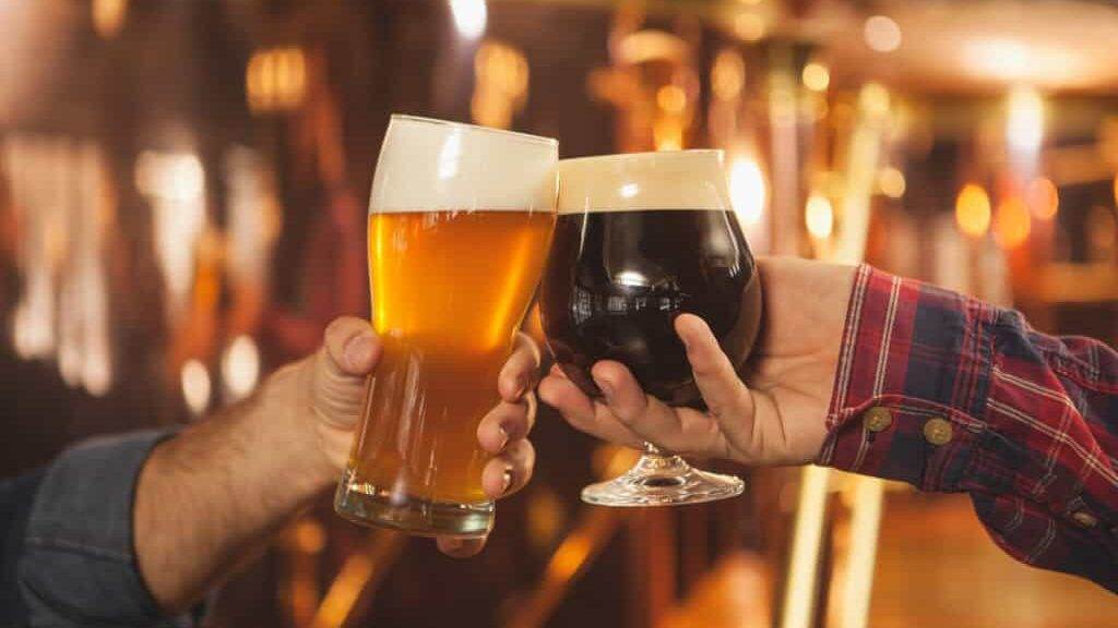 Cropped close up of two men clinking beer glasses together, celebrating at the beer pub. Professional brewers toasting with their beer glasses. Success celebration, oktoberfest festival concept
