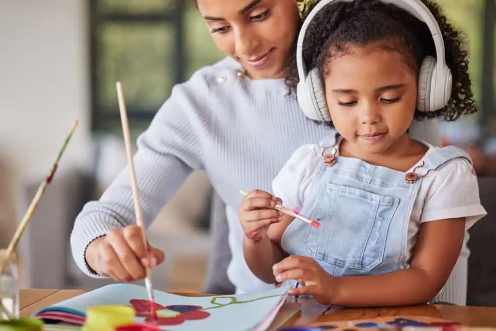 Mother, girl and bonding in painting activity with music headphones, radio or audio for autism help. Brazilian woman, art parent and creative child listening to relax autism podcast in house or home.