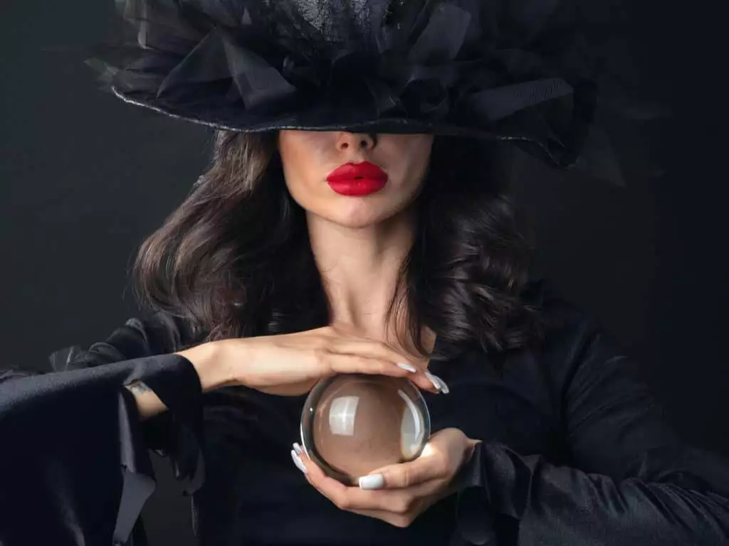 Beautiful sexy model woman in Halloween witch costume holding crystal ball putting spell fortune telling