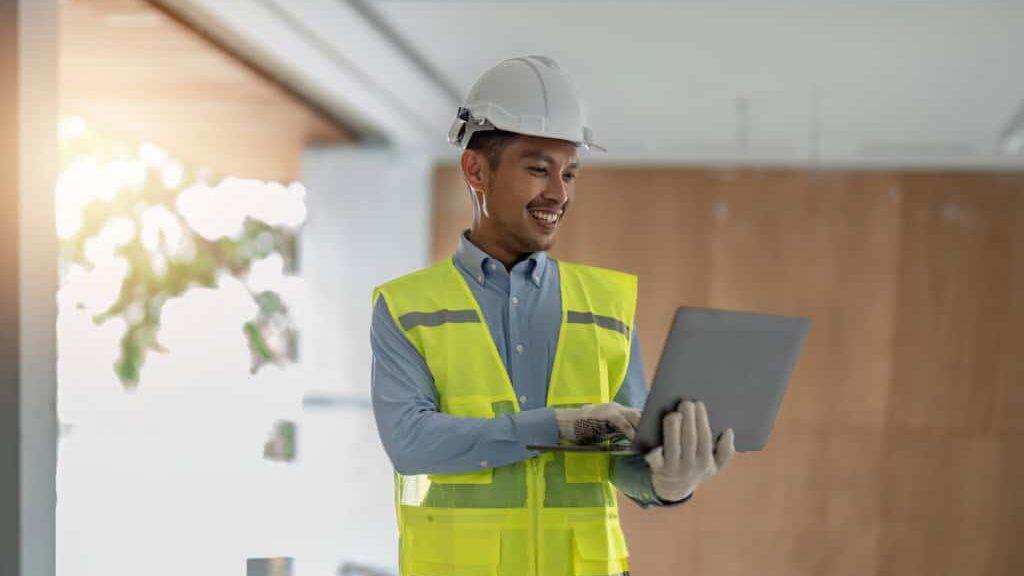 A man in a hard hat holding a laptop.