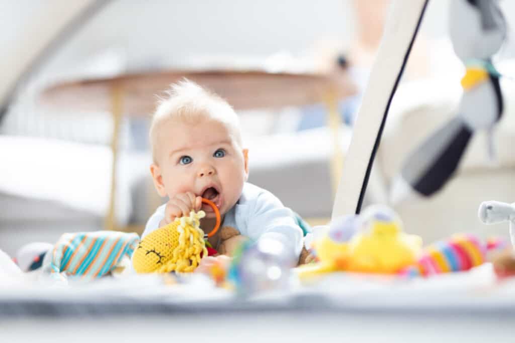Cute baby boy playing with hanging toys arch on mat at home Baby activity and play center for early infant development. Baby playing at home.