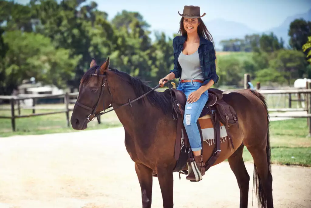 A woman in a cowboy hat sits on a brown horse.