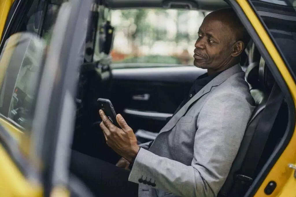 Contemplative black businessman using smartphone in taxi