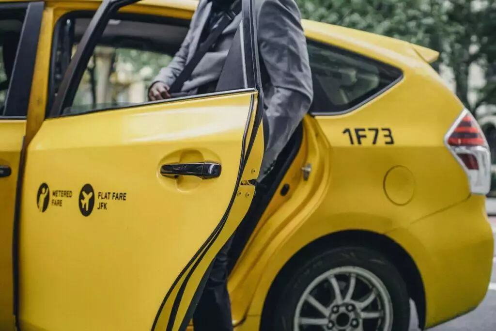 Black man in elegant suit opening door of yellow taxi
