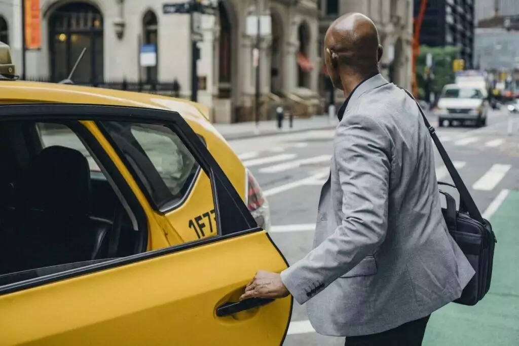 Faceless black man opening taxi door on busy street