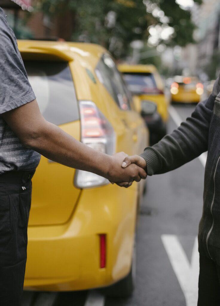Side view of crop faceless ethnic males having handshake concluding agreement standing on road near taxi