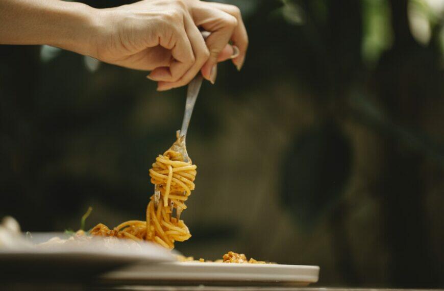 Crop anonymous female rolling delicious spaghetti with tomato sauce on fork during dinner in restaurant