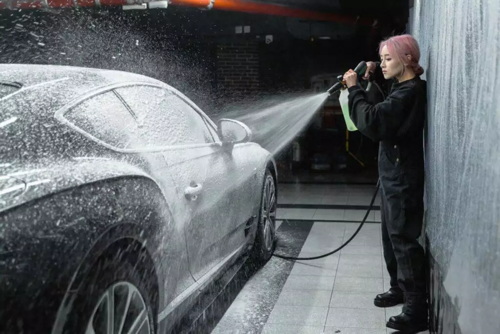 A Woman in a Black Sweater Spraying Soap on a Car