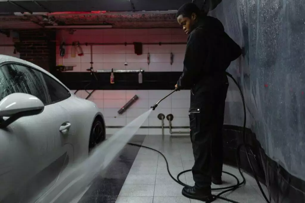 Man in Black Jacket Cleaning the White Car Parked on a Garage